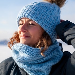 Frau mit Mütze reckt in Winterlandschaft das Gesicht in die Sonne:  Licht beeinflusst fast alle Bereiche unseres Lebens. Die Interaktion von Licht und Farbe prägt unmittelbar unsere Wahrnehmung. 
