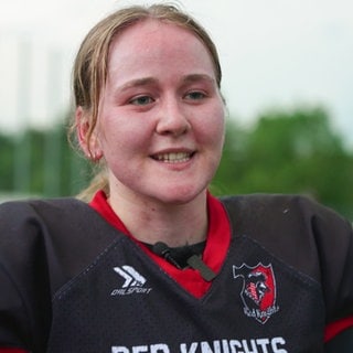 American Football-Spielerin Sophie Hausch steht auf einem Sportplatz und trägt eine schwarze Football-Uniform. Ihr Gesischt ist rot und leicht verschwitzt vom Training.