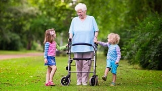 Eine ältere Frau mit Rollator und ihren Enkelkindern im Park