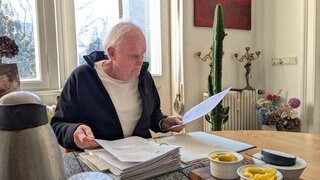Karl Eugen Bleyler sitzt an seinem Wohnzimmertisch und blättert seine Bescheide zur Grundsteuer durch. 