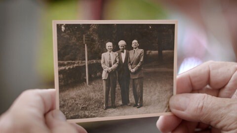 Zwei Hände halten ein altes Foto von 3 Brüdern
