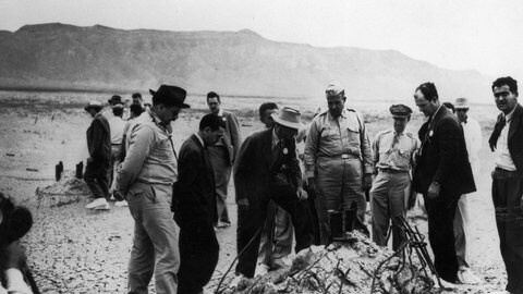 Mitwirkende des Manhattan-Projekts, darunter Dr. Robert J. Oppenheimer (Mann mit weißem Hut) und neben ihm General Leslie Groves, inspizieren die Detonationsstelle des Trinity-Atombombentests.