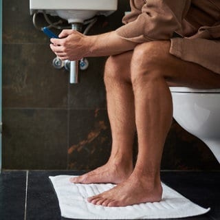 Mann mit Handy auf dem Klo