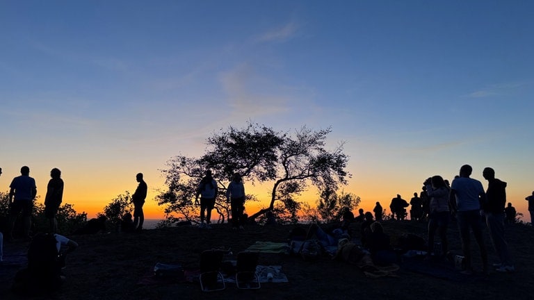 Vor einem abendlich erleuchteten Himmel laufen mehrere Menschen als Schatten erkennbar entlang.