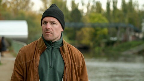 Junger Mann mit Mütze steht am Rhein