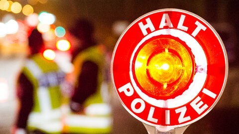  Ein Polizist hält bei einer Verkehrskontrolle eine rote Kelle mit der Aufschrift "Halt Polizei" hoch
