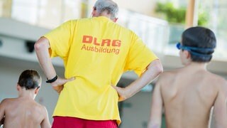 Ein Schwimmlehrer der DLRG steht am Beckenrand und bringt Kindern das Schwimmen bei.
