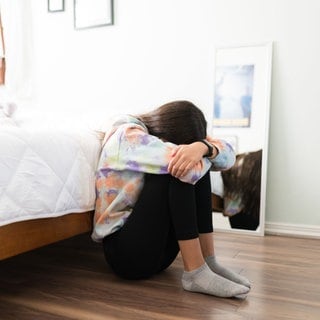 Junge Frau hockt verzweifelt vor ihrem Bett