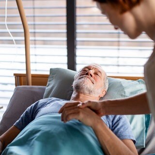 Ein Patient liegt nach einer OP im Bett: Nicht nur ältere Menschen, sondern auch junge oder Säuglinge können nach einer Narkose in einen Zustand des Delirs geraten. Sie sind verwirrt und körperlich unruhig, haben Halluzinationen oder Wahnvorstellungen. Das kann bei Erwachsenen Stunden und Tage nach dem Erwachen auftreten und Tage andauern. Kognitive Beeinträchtigungen können folgen. 