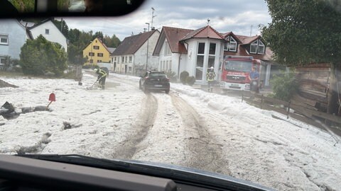 Weiße Straßen in Schemmerberg: Ein Feuerwehrmann ist im Einsatz, um Hagelkörner von der Straße zu beseitigen.