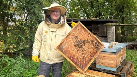 Platzansager Christian hält in Imkerkluft seine Bienen in die Kamera und lacht. 
