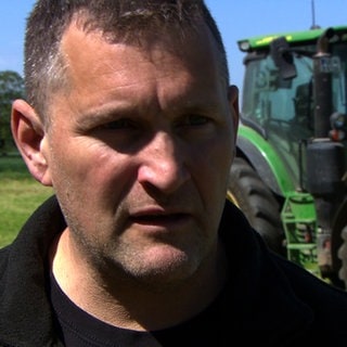 Landwirt Thomas Frenk steht vor seinem Traktor. Er hat Rattengift in seiner Heuwiese gefunden.