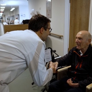 Arzt spricht mit älterem Patient im Rollstuhl