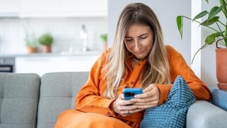 Eine Frau sitzt auf der Couch und ist in ihr Smartphone vertieft | Nutzen wir das Smartphone weniger, werden wir kreativer