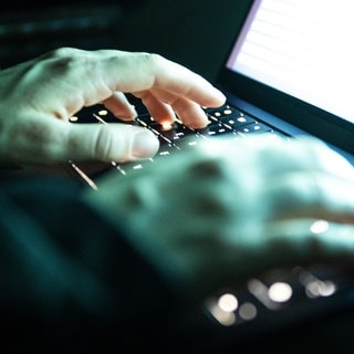 Eine Person tippt mit den Fingern auf einer beleuchteten Laptop-Tastatur (Symbolbild).