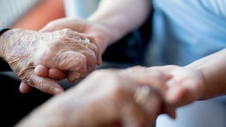 Eine Pflegekraft hält einem alten Menschen die Hand.