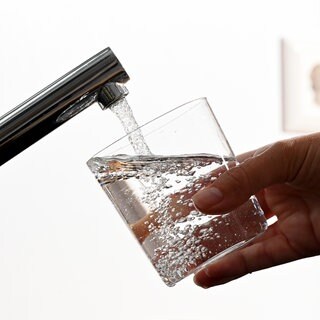 Eine Hand hält ein Wasserglas unter einen Wasserhahn.