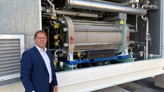 Projektleiter Alexander Sauer von der Uni Stuttgart vor einer Maschine, die Wasserstoff produziert