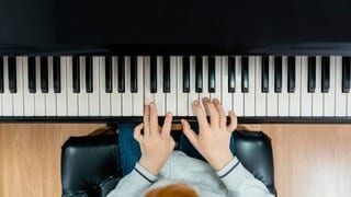 Ein Kind übt Klavier: Früher hatte die Tastatur des Instruments keine schwarzen Tasten; sie bestand nur aus den heute weißen Tasten. Wie kam es zur Entwicklung?