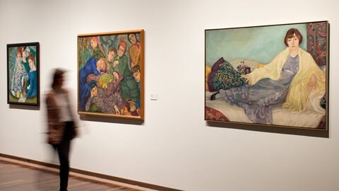 Frau geht an Bildern in einer Ausstellung vorbei