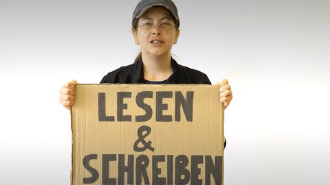 Eine Frau hält ein Schild auf dem "Lesen und Schreiben" steht. Mehr dazu in der ARD Themenwoche 2022