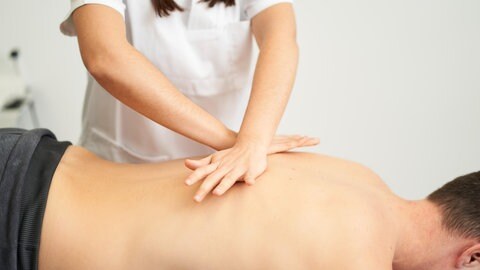 Eine Frau in weißer Kleidung drückt mit den Händen auf den Rücken eines vor ihr liegenden Mannes. Behandlungen in der Osteopathie sehen häufig aus wie Massagen. Ihre Wirksamkeit ist umstritten.