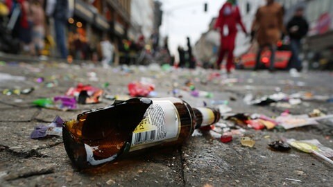 Eine kaputte Bierflasche liegt an Fastnacht umringt von Konfetti auf einem Kopfsteinpflaster.