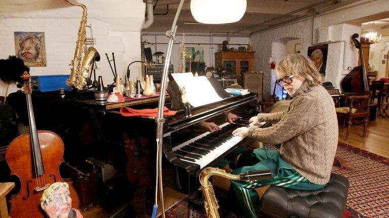 Helge Schneider sitzt am Piano, umgeben ist er von schier unzähligen Instrumenten. 