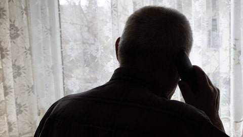 Älterer Mann steht mit einem Telefon vor dem Fenster