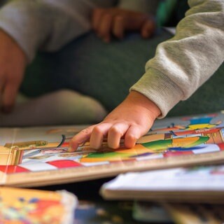 Ein Kita-Kind liest zusammen mit einer Erzieherin ein Buch.