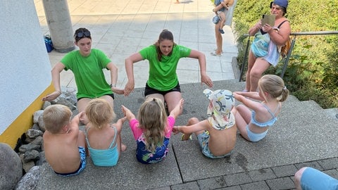 Zwei Schwimmlehrerinnen zeigen den Kindern die richtigen Bewegungen.