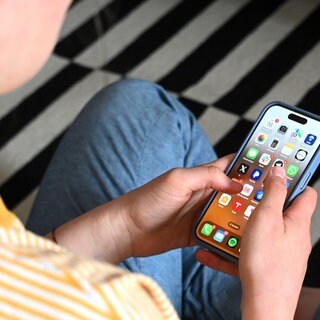 (Symbolbild zu Cybergrooming): Eine Jugendliche sitzt auf dem Boden und nutzt ein Smartphone - auf dem Display sind verschiedene Apps zu sehen.