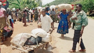 12. April 1994: Angehörige der Hutu fliehen südlich von Kigali vor den schweren Kämpfen zwischen den Regierungstruppen der Hutu und den Rebellen der Rwanda Patriotic Front (RPF) der Tutsi. Der Mann rechts ist Zivilist, Hutu und arbeitet auf der Seite der Regierungstruppen. Er kontrolliert die Flüchtlinge um sicherzustellen, dass keine Tutsi darunter sind. Hunderttausende Menschen fliehen nach dem Mord am Präsidenten Ruandas am 6. April 1994 vor den Massakern in Kagali und Umgebung. 
