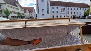 Ein Handy wird in einen Sarg gelegt. Das ist Teil einer Ausstellung in der Johanniskirche in Schwäbisch Gmünd. Es geht dabei auch um Digital Detox.