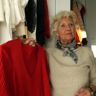Sabine Lynch steht vor ihrem Kleiderschrank und zeigt ein rotes Kleid.