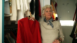 Sabine Lynch steht vor ihrem Kleiderschrank und zeigt ein rotes Kleid.