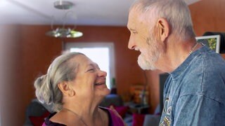 Michael und Ulrike sind ein weißes Paar mit grauen Haaren. Sie lachen sich gegenseitig an.