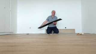 Ein Mann kniet in einem leeren Raum. Er verlegt Laminat.