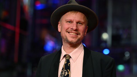 Robert Stadlober hat einen Hut auf und lacht in Richtung Kamera