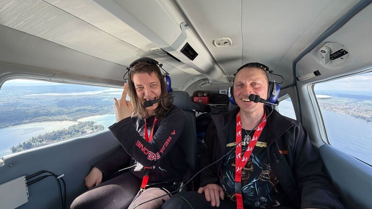 Marleen und ihr Verlobter Matthias sitzen im Flugzeug. Durch die Fenster ist der Bodensee zu sehen.