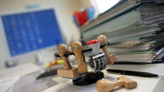 Schreibtisch in einer Behörde mit Stempeln und Akten (Symbolbild): Laut Rechnungshof haben zwei Kommunen insgesamt fünf Beschäftigte rechtswidrig über Jahre hinweg bei voller Bezahlung von der Arbeit freigestellt.