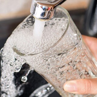 Ein Glas wird unter einem Wasserhahn befüllt. 