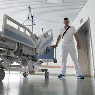 Florian steht rechts im Bild neben einem Patientenbett. Er trägt weiße Kleidung.
