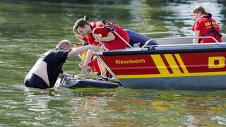 DLRG-Retter zeigen bei einer Übung, wie sie mit dem Boot einen erschöpften Schwimmer aus dem Wasser helfen.  Nur 43 Prozent trauen sich zu, jemanden vor dem Ertrinken zu retten, sagt die DLRG. Wir klären die wichtigsten Fragen rund um das Thema "Unfälle und Sicherheit beim Baden" und geben euch Tipps, wie ihr euch im Notfall richtig verhaltet - und wie nicht.