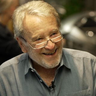 Mann mit grauen Haaren und Brille lächelt.