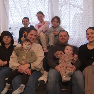 Die neunköpfige Familie Bajgora sitzt gemeinsam auf dem Sofa und lächelt in die Kamera.
