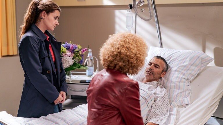 Jenny (Julia Obst) und Bea (Christiane Brammer) stehen an Manuels (Marco Canadea) Krankenbett