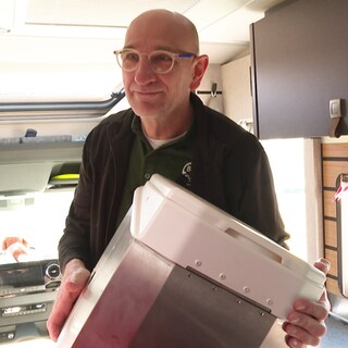 Sascha Gerner hat seine selbsterfundene Campingtoilette in der Hand. Er steigt in einen Campingwagen. 