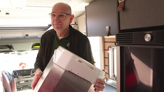 Sascha Gerner hat seine selbsterfundene Campingtoilette in der Hand. Er steigt in einen Campingwagen. 