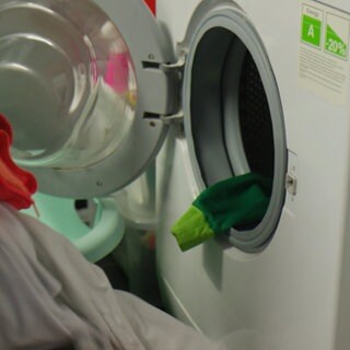 Eine offene Waschmaschine wird mit bunter Wäsche befüllt
